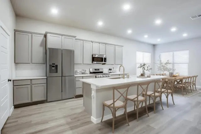 a large kitchen with kitchen island a sink dishwasher a stove a refrigerator and white cabinets with wooden floor