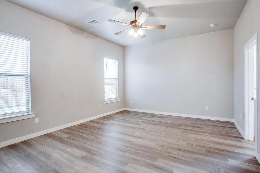 10502 Aberdeen Avenue Lubbock, TX 79424 - Photo 9 of 20 an empty room with wooden floor chandelier fan and windows