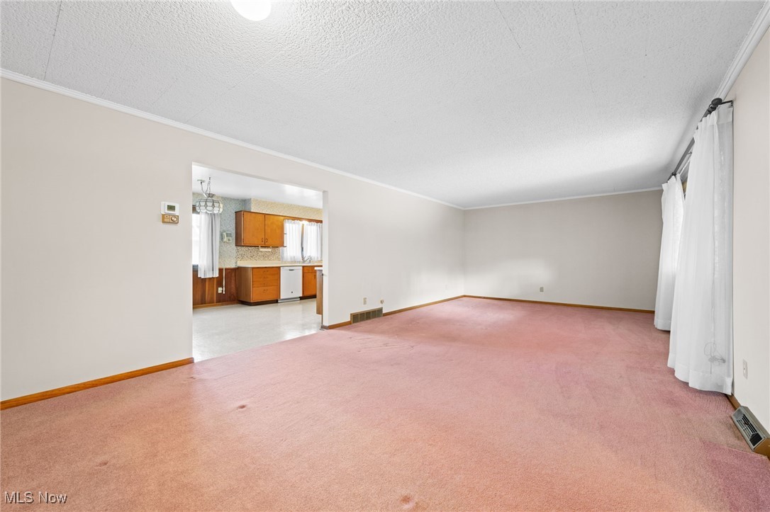 Unfurnished living room featuring baseboards, light carpet, visible vents, and a textured ceiling