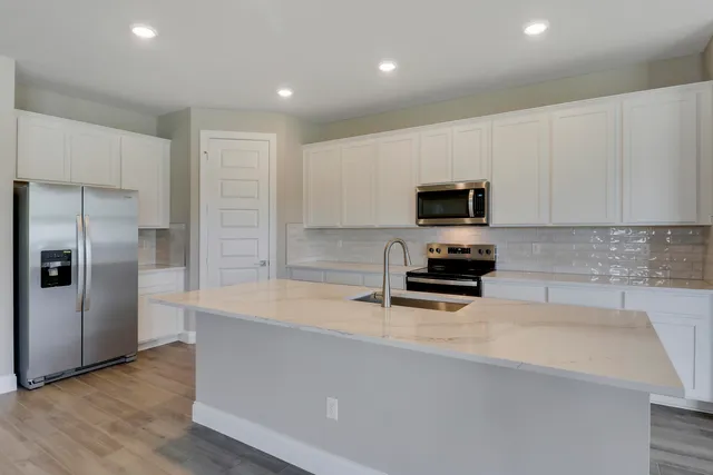 a large white kitchen with kitchen island a stove a sink a refrigerator and grey cabinets with wooden floor