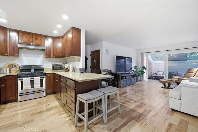 a kitchen with stainless steel appliances granite countertop a stove top oven a sink dishwasher a dining table and chairs with wooden floor