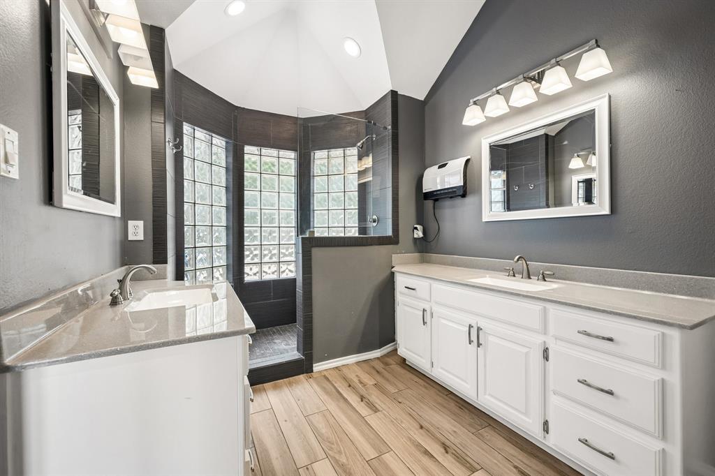 1380 Meandro Ria Lane Fairview, TX 75069 - Photo 20 of 39 Dual vanity sinks with white cabinetry, wood-finish flooring, and a glass block shower enclosure with dark tile
