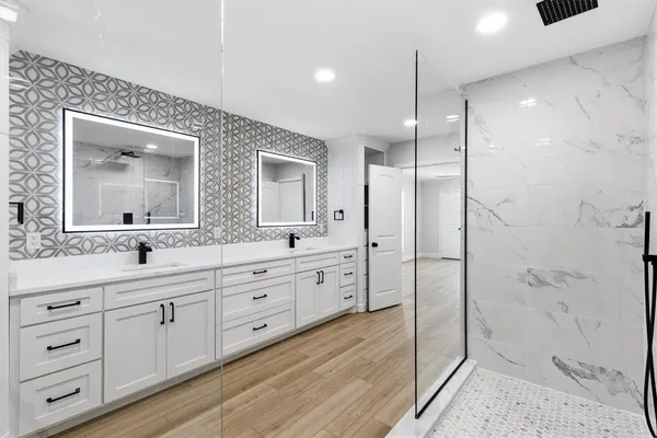a spacious bathroom with double vanity a mirror and a shower