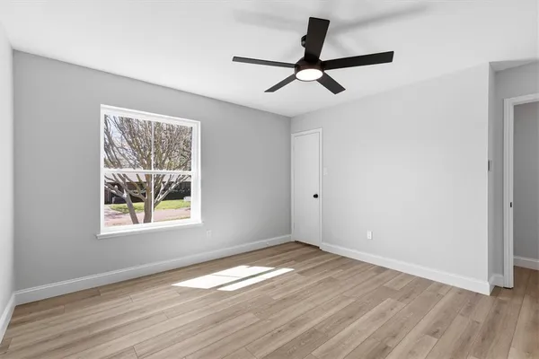 an empty room with wooden floor ceiling fan and windows