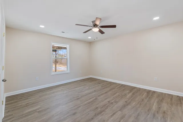a view of an empty room with wooden floor and a ceiling fan