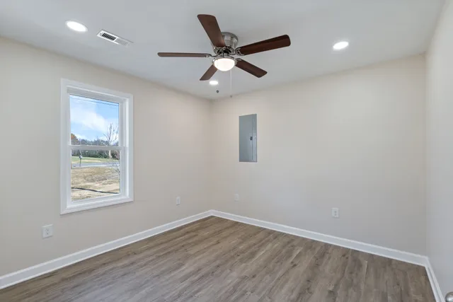 an empty room with wooden floor ceiling fan and windows