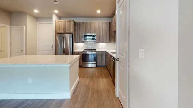 a large kitchen with a large counter top a refrigerator and wooden cabinets