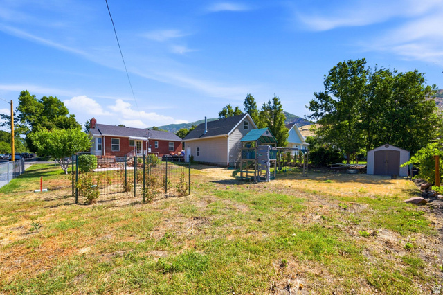 310 East 600 South Centerville, UT 84014 - Photo 29 of 41 Expansive backyard featuring a red brick dwelling with a patio, a detached beige accessory structure, a fenced garden area, and a metal storage shed