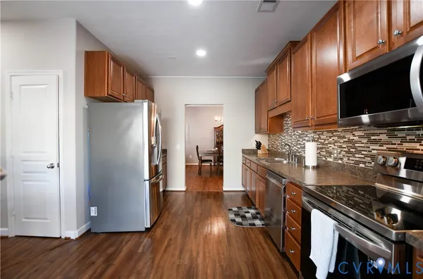 a kitchen with stainless steel appliances granite countertop a stove top oven a refrigerator a sink and dishwasher with wooden floor