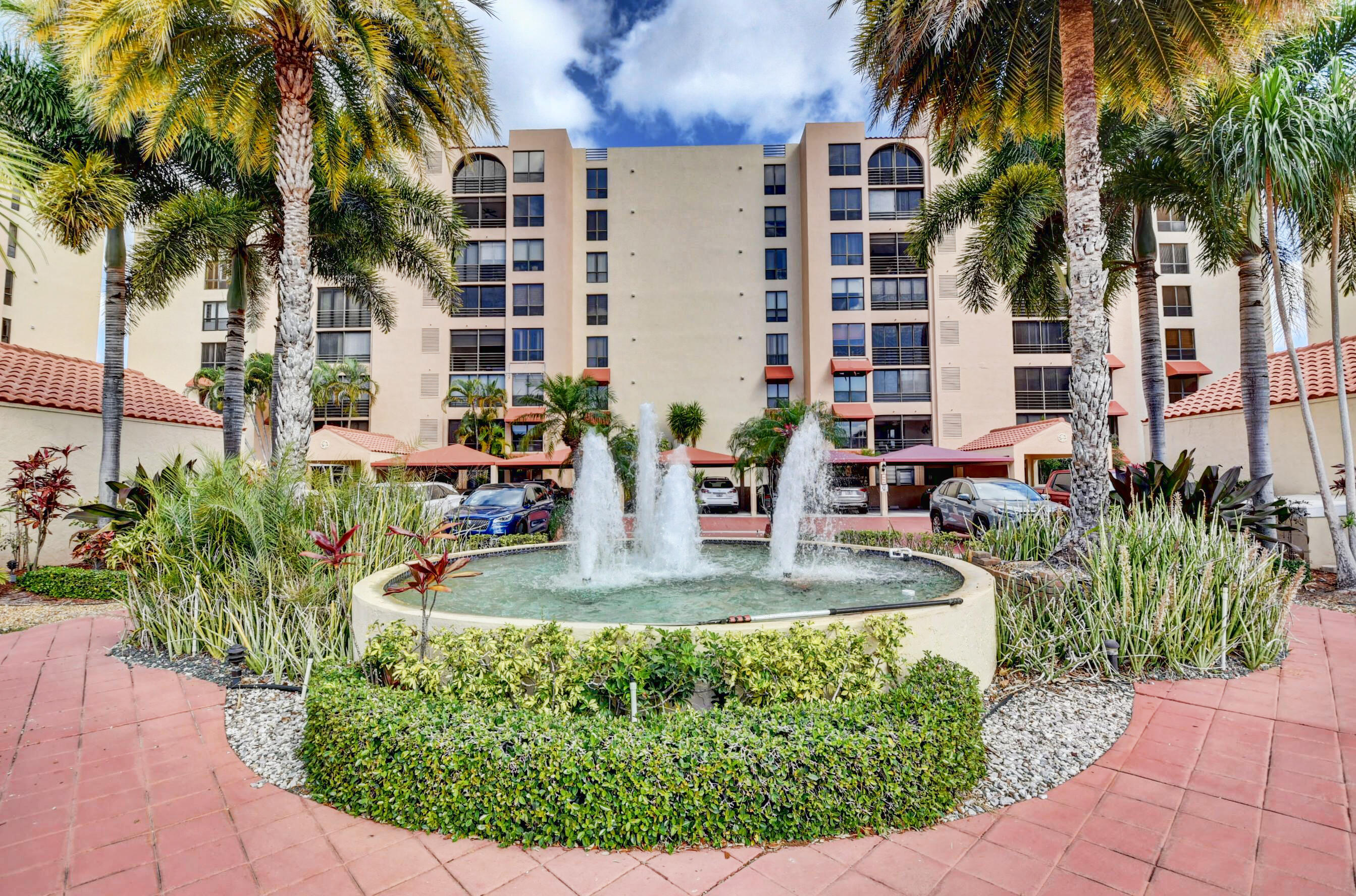 a view of a tall building with a fountain and a lawn chair under palm trees