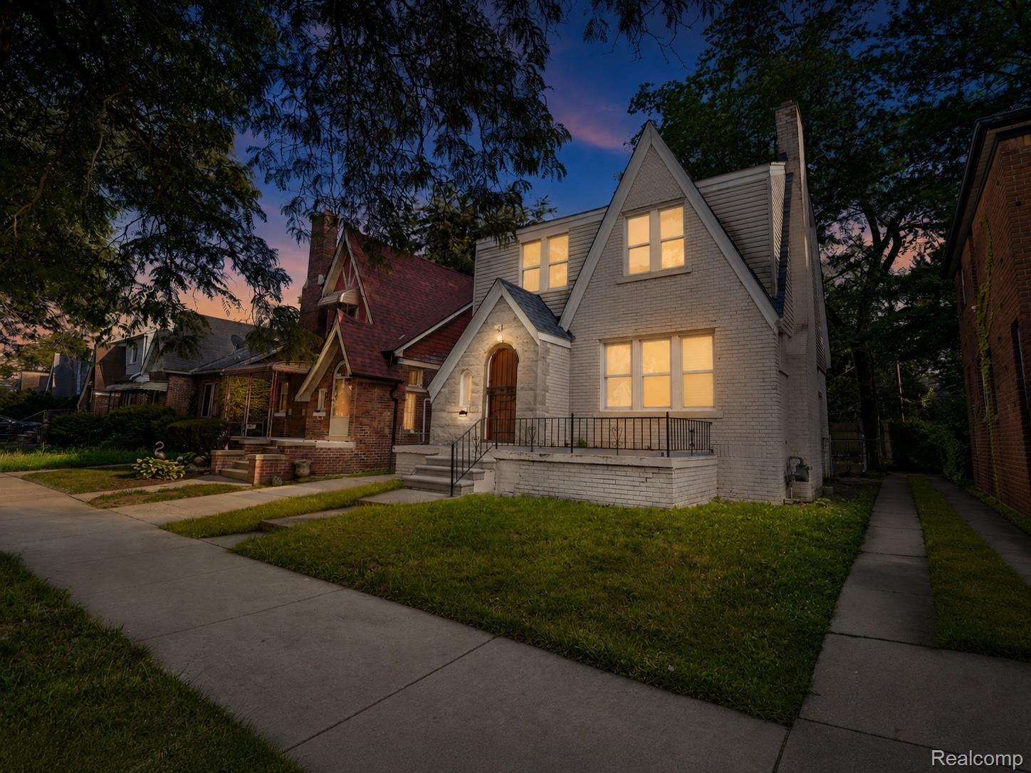 9175 Devonshire Road Detroit, MI 48224 - Photo 2 of 23 Gabled-roof residence featuring light-colored brick and siding, a stone entryway with an arched wooden door, and a wrought-iron railing