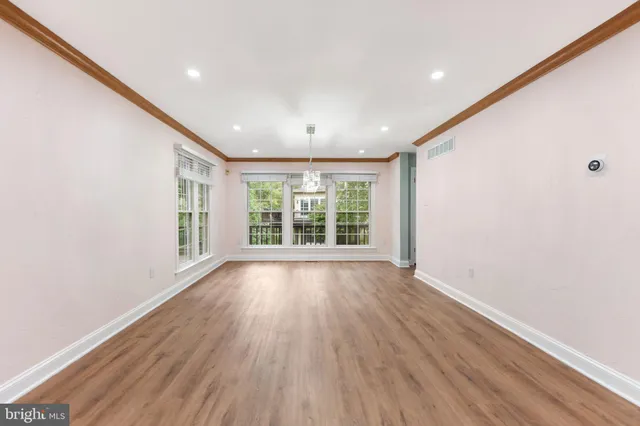 a view of an empty room with wooden floor and a kitchen