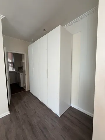 a view of an empty room with wooden floor and a kitchen
