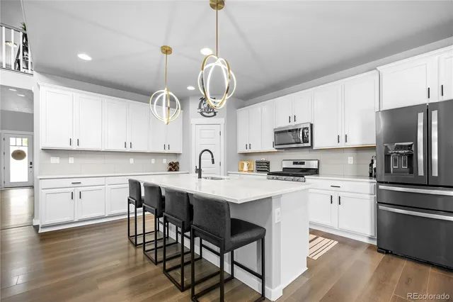 a kitchen with stainless steel appliances granite countertop a sink a stove a oven a refrigerator a dining table and chairs with wooden floor