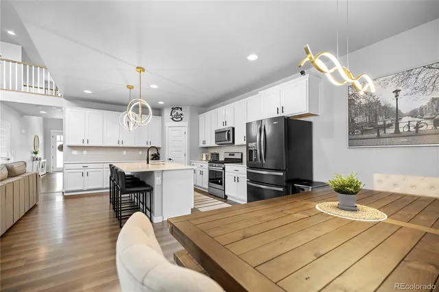 a kitchen with stainless steel appliances kitchen island granite countertop a refrigerator a stove a sink dishwasher and a dining table with wooden floor