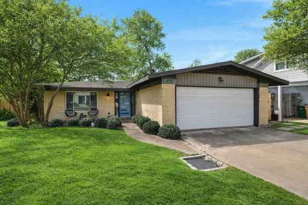 a view of a house with a yard plants and large tree