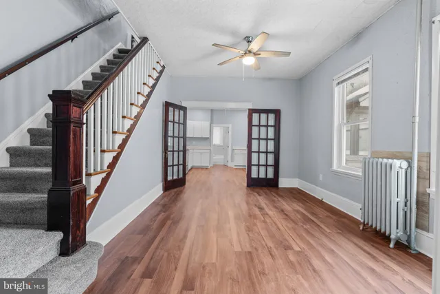 a view of an empty room with wooden floor and fan