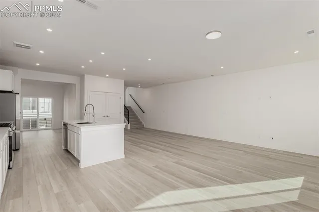 a large white kitchen with kitchen island a stove a sink dishwasher and white cabinets with wooden floor