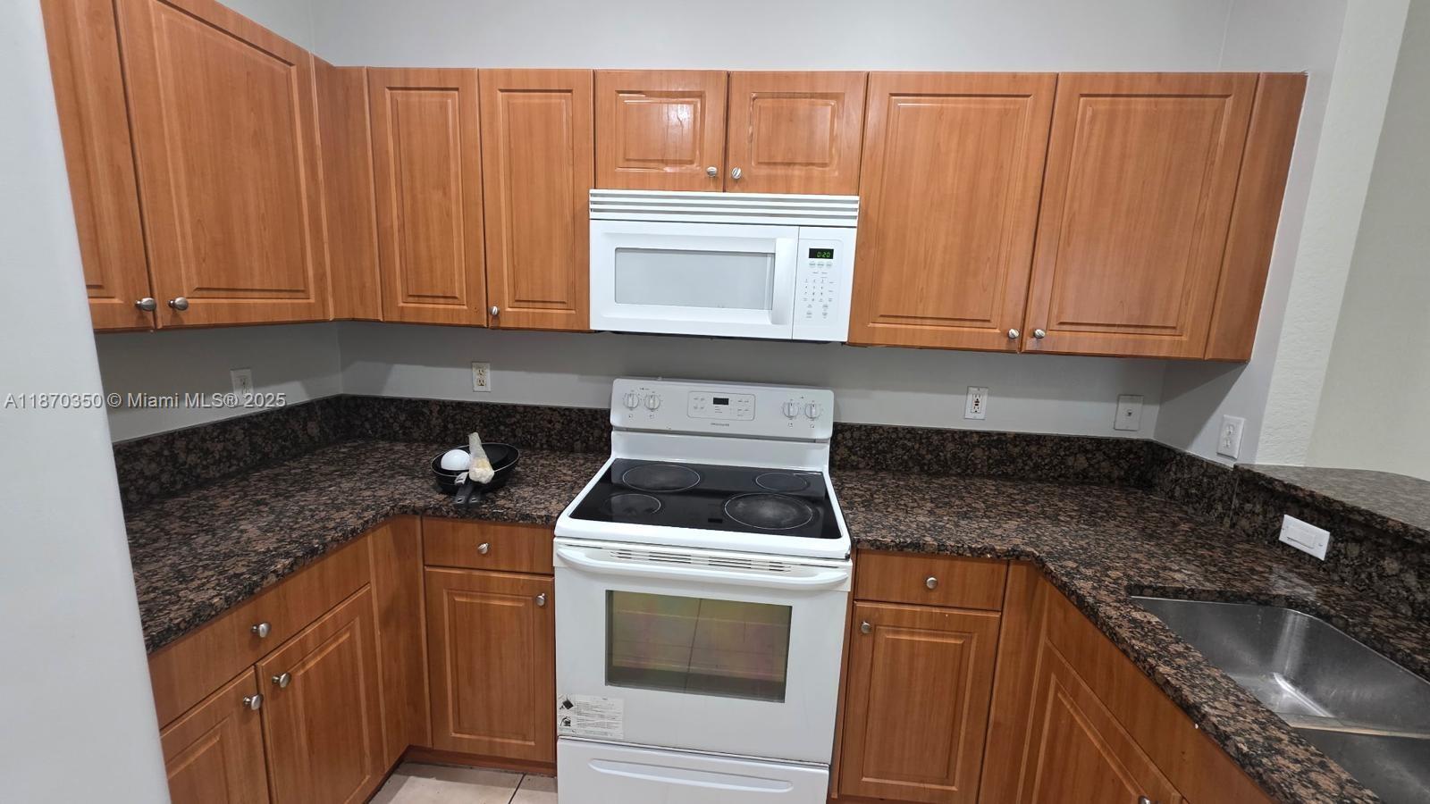 2748 Southwest 83rd Avenue, Unit 108 Miramar, FL 33025 - Photo 4 of 20 a kitchen with granite countertop wood cabinets and white appliances