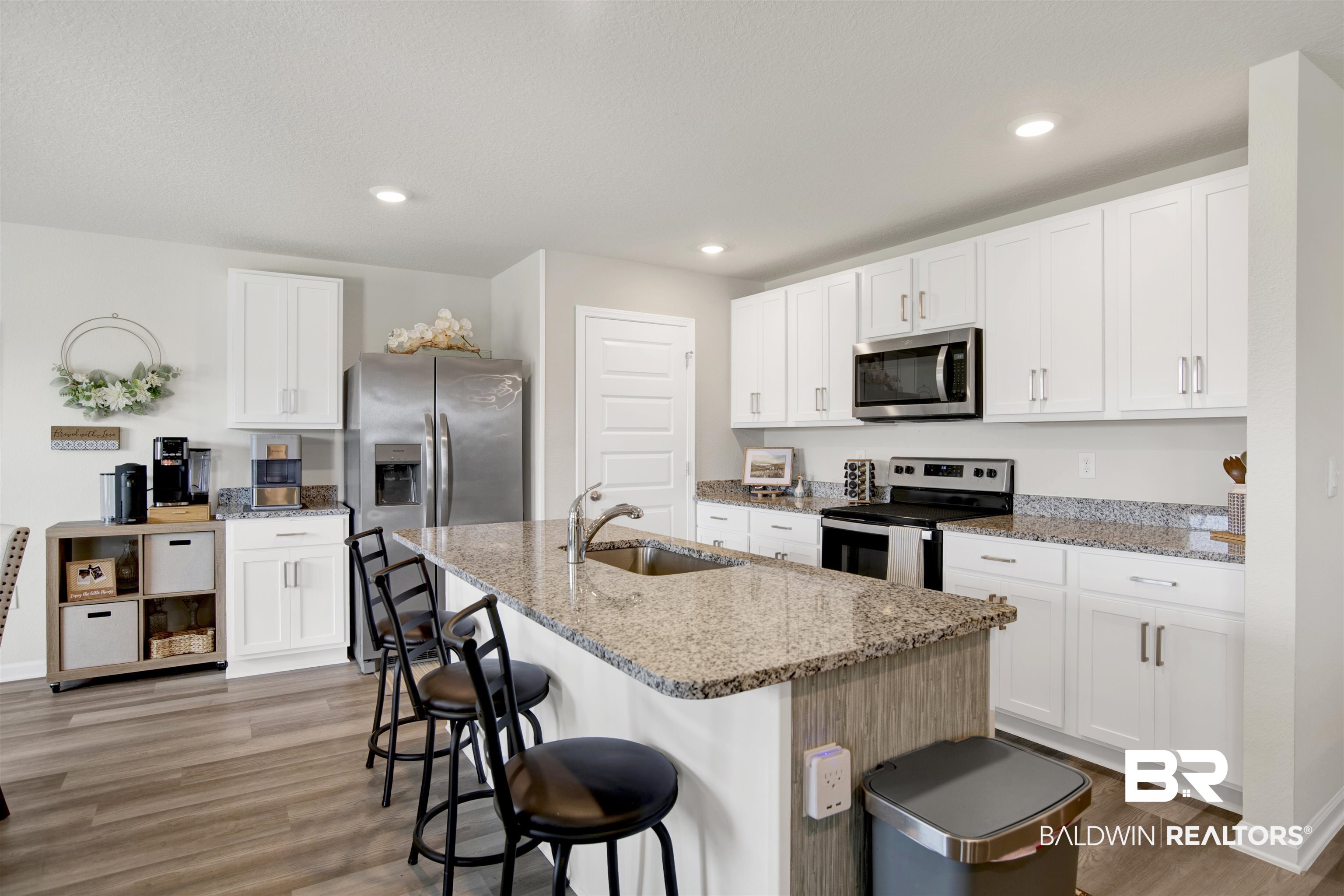 22301 Early Dawn Circle Foley, AL 36535 - Photo 24 of 45 Kitchen featuring an island with a built-in sink, white cabinetry, stainless steel appliances, wood-finish flooring, and granite countertops