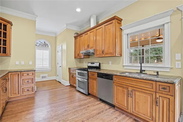 a kitchen with stainless steel appliances granite countertop wooden cabinets a stove a sink and dishwasher with wooden floor