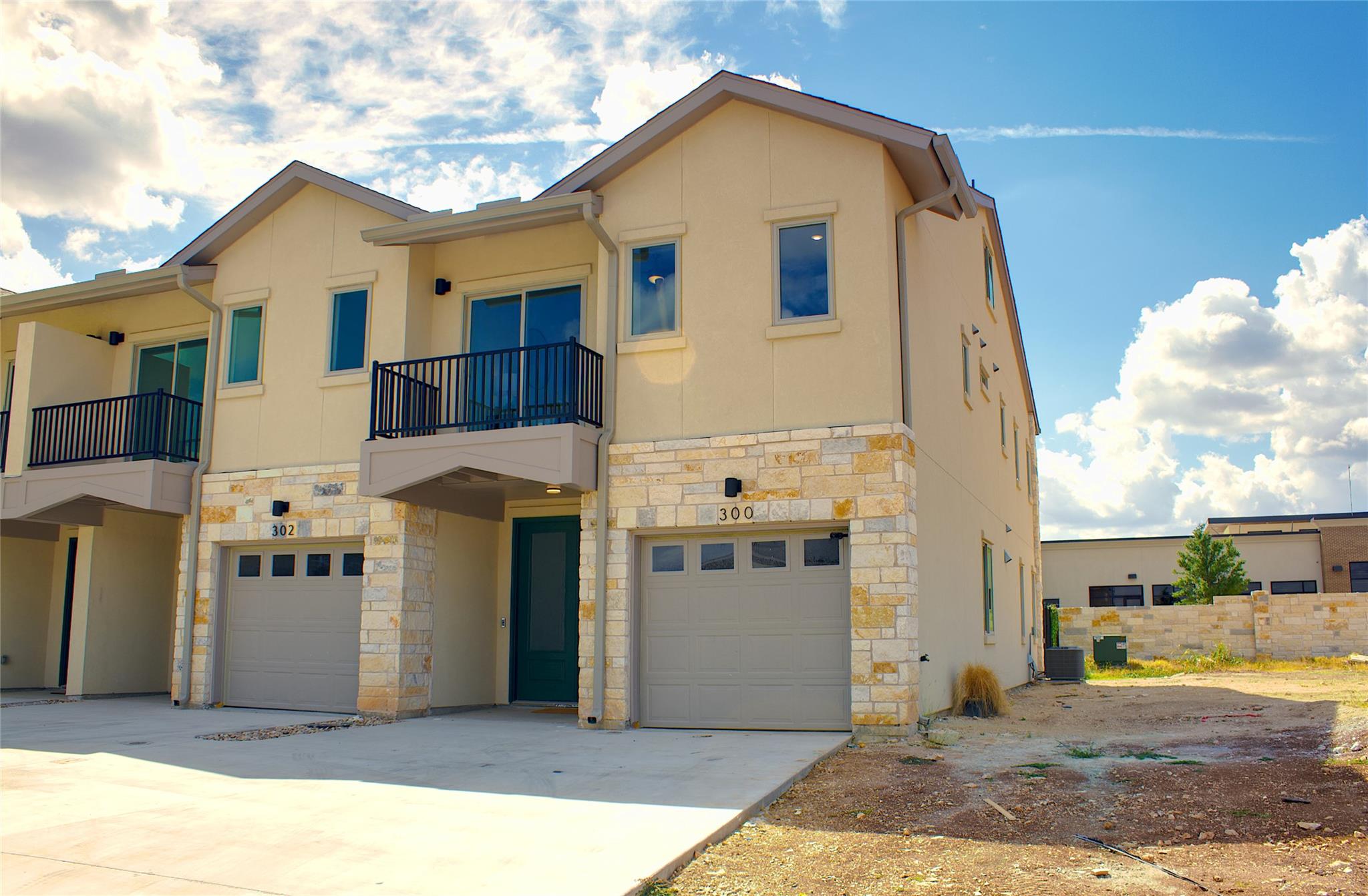 Contemporary townhome exterior featuring light-colored stucco and natural stone veneer