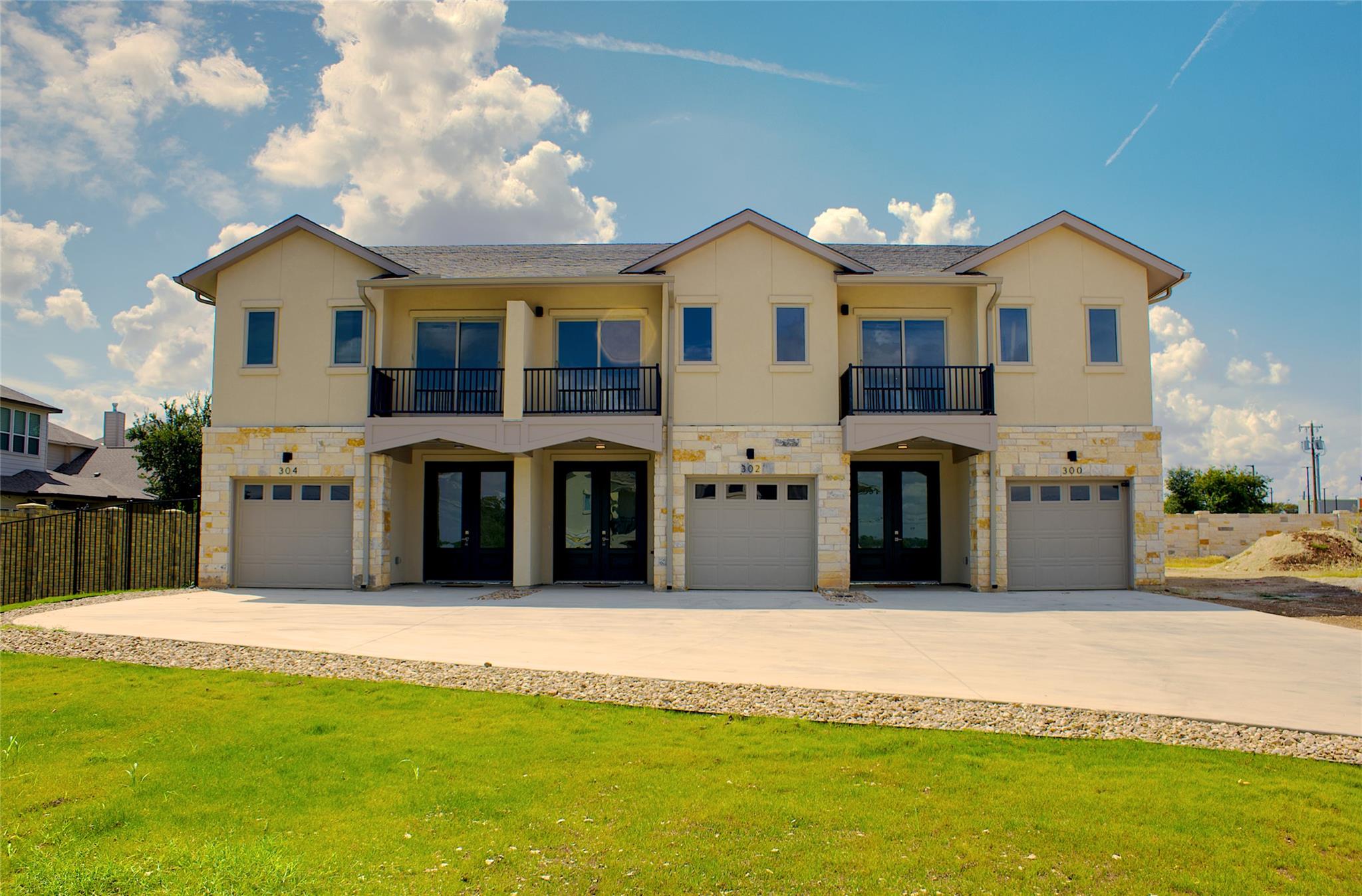 300 Tesla Circle Austin, TX 78681 - Photo 2 of 39 Contemporary townhouse exterior featuring a stucco and stone facade, private balconies with black railings, individual garage doors, and a concrete driveway