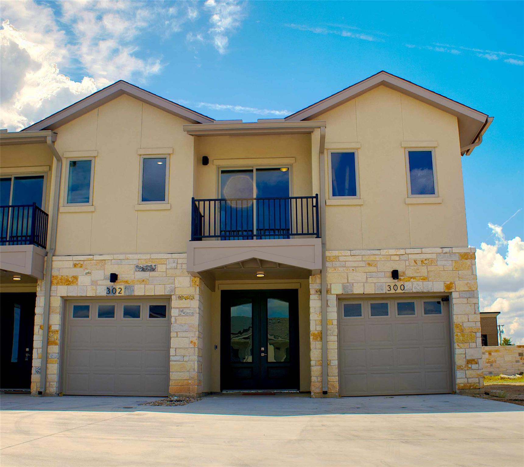 300 Tesla Circle Austin, TX 78681 - Photo 3 of 39 Contemporary stucco and stone exterior featuring a private balcony with black metal railing, dual arched entry doors, and two single-car garages