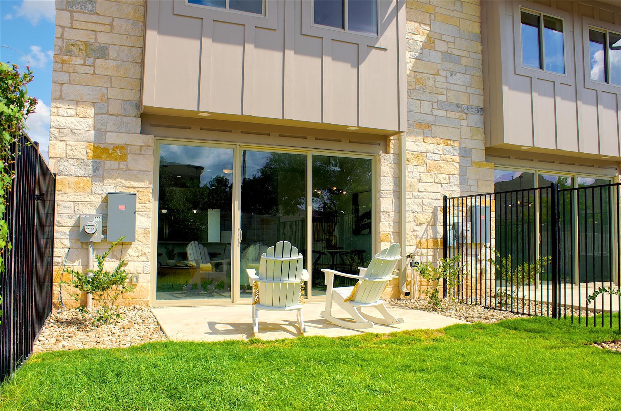 300 Tesla Circle Austin, TX 78681 - Photo 34 of 39 Outdoor patio area with a stone and panel exterior, featuring sliding glass doors, a manicured lawn, and a black wrought iron fence