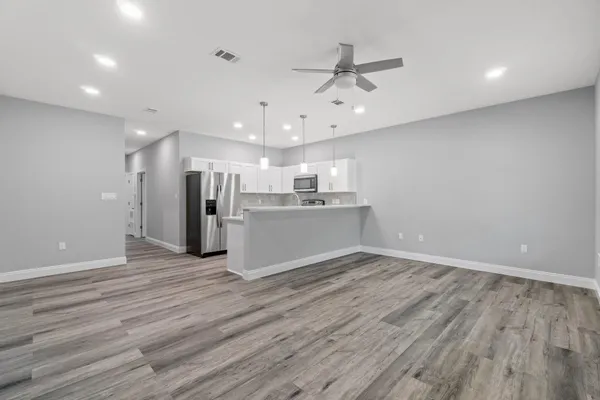 an empty room with wooden floor chandelier fan and windows