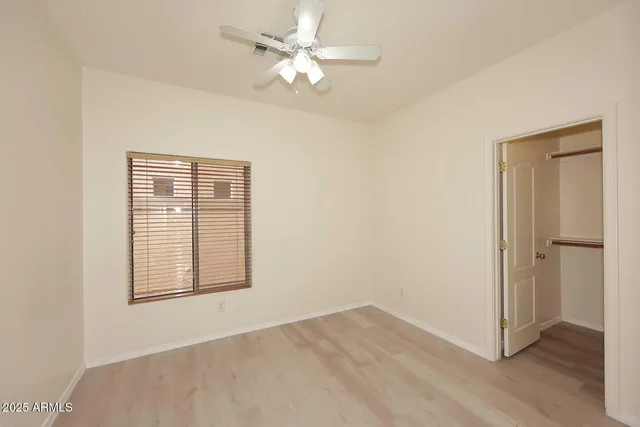 an empty room with wooden floor chandelier fan and windows