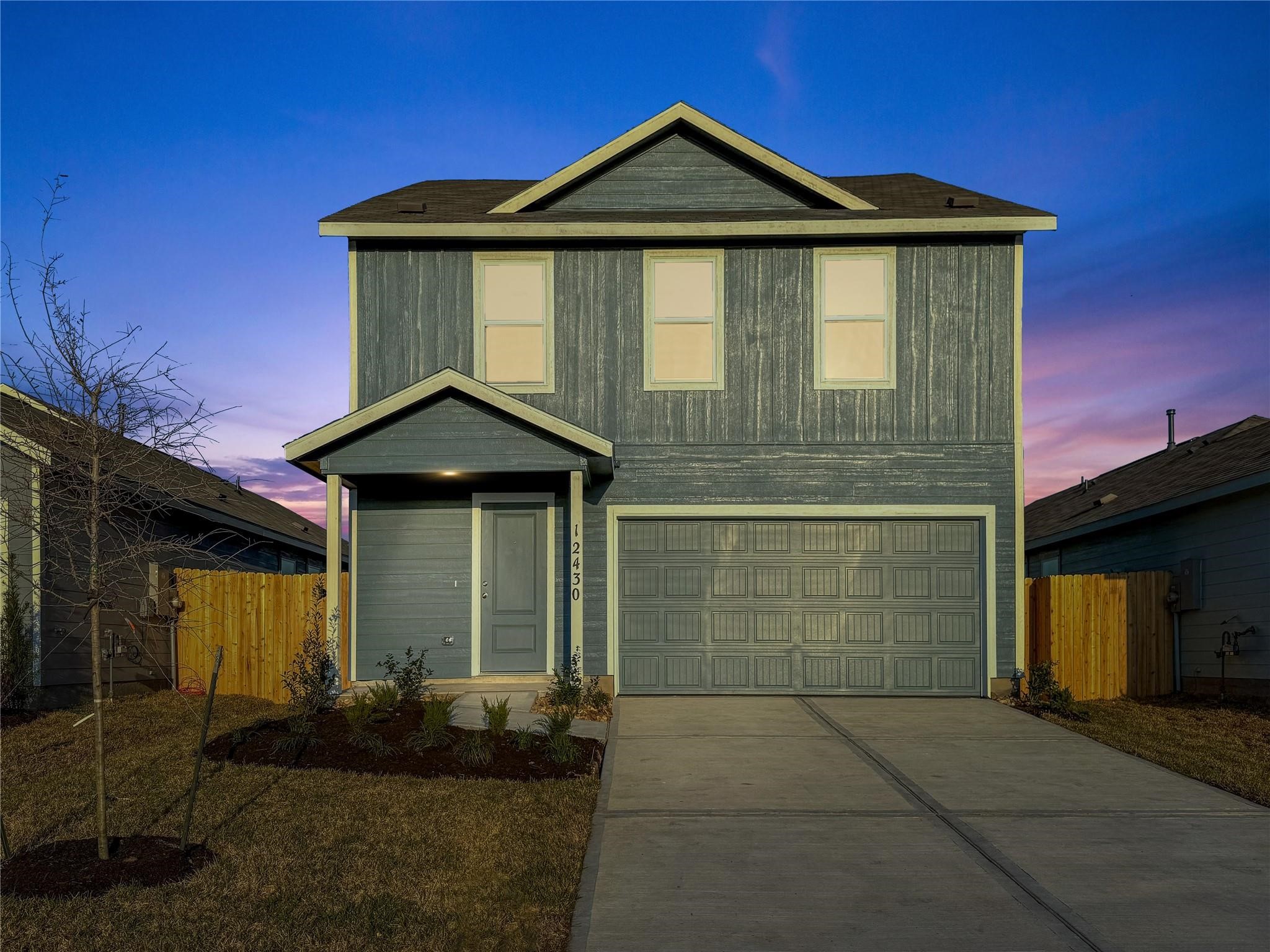 12430 Wild Strawberry Road Houston, TX 77038 - Photo 2 of 34 This modern two-story home features a sleek gray exterior, a two-car garage, and a covered entryway. The neatly maintained front yard offers simple landscaping, beautifully complemented by a vibrant twilight sky.