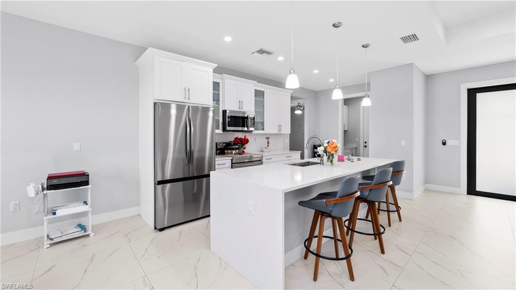4571 22nd Street Northeast Naples, FL 34120 - Photo 11 of 47 Kitchen featuring stainless steel appliances, glass insert cabinets, a kitchen breakfast bar, light marble finish floors, and white cabinets