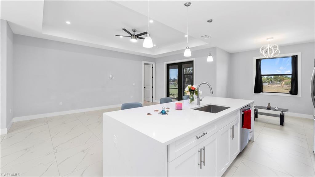 4571 22nd Street Northeast Naples, FL 34120 - Photo 12 of 47 Kitchen featuring a kitchen island with sink, a raised ceiling, light stone countertops, hanging light fixtures, and white cabinetry