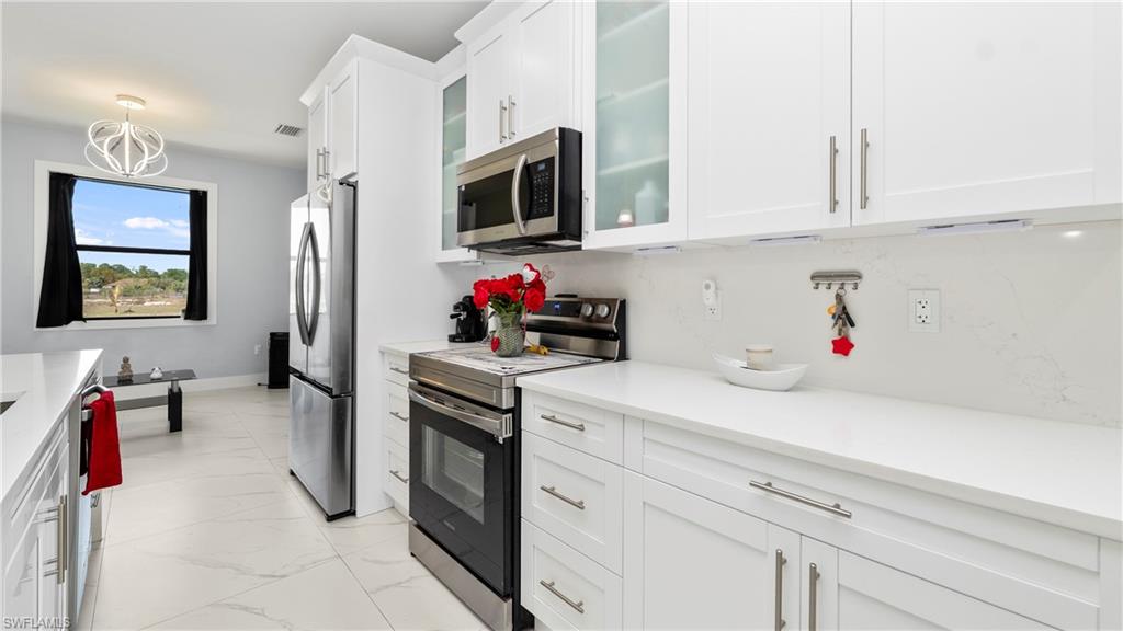 4571 22nd Street Northeast Naples, FL 34120 - Photo 14 of 47 Kitchen featuring stainless steel appliances, glass insert cabinets, white cabinets, light marble finish flooring, and light stone countertops