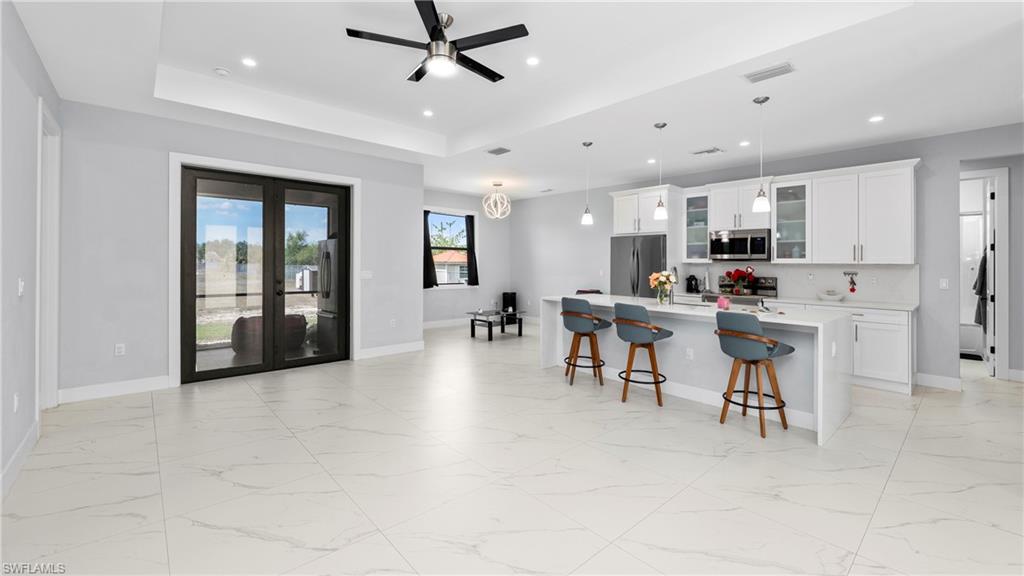 4571 22nd Street Northeast Naples, FL 34120 - Photo 8 of 47 Kitchen with white cabinetry, glass fronted cabinets, light marble finish flooring, ceiling fan, and a breakfast bar area