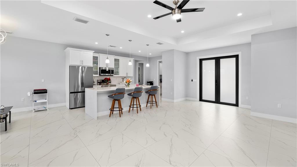 4571 22nd Street Northeast Naples, FL 34120 - Photo 10 of 47 Kitchen with light marble finish flooring, an island with sink, stainless steel appliances, a kitchen breakfast bar, and glass insert cabinets