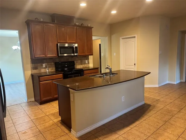 a kitchen with kitchen island granite countertop a sink and a stove top oven with wooden cabinets