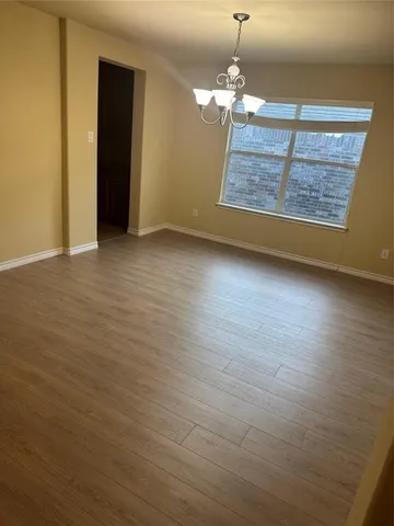 an empty room with wooden floor chandelier and windows