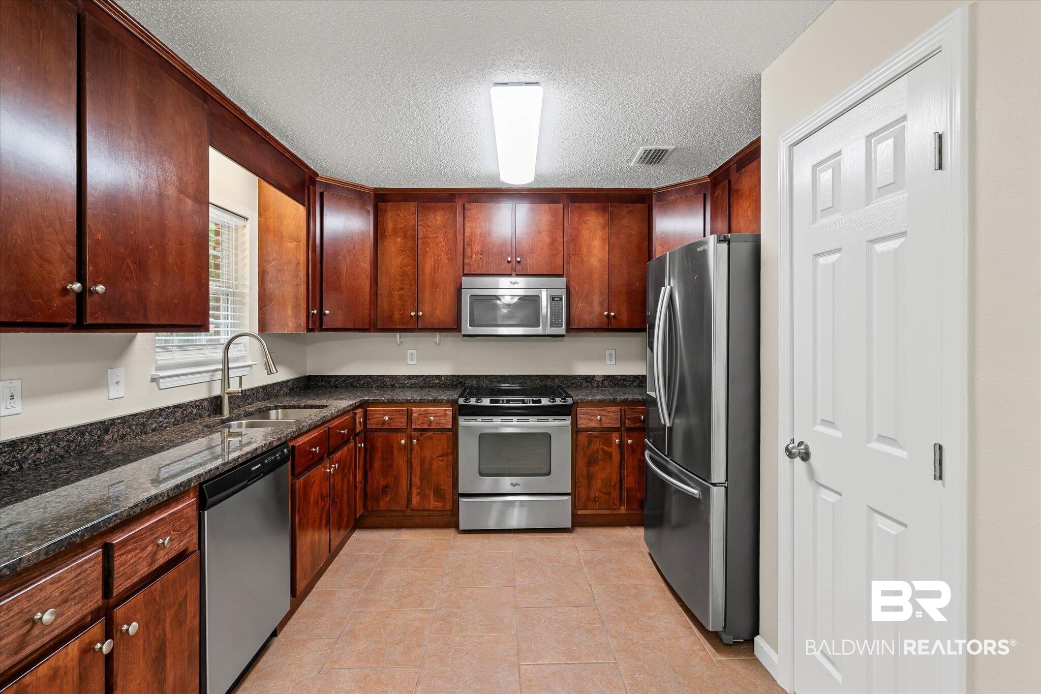 157 Bay View Drive Daphne, AL 36526 - Photo 5 of 22 Kitchen with dark stone countertops, appliances with stainless steel finishes, a textured ceiling, and light tile patterned floors