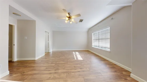 a view of an empty room with wooden floor and a chandelier fan