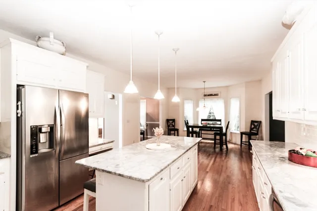 a kitchen with stainless steel appliances kitchen island granite countertop a dining table chairs and a refrigerator