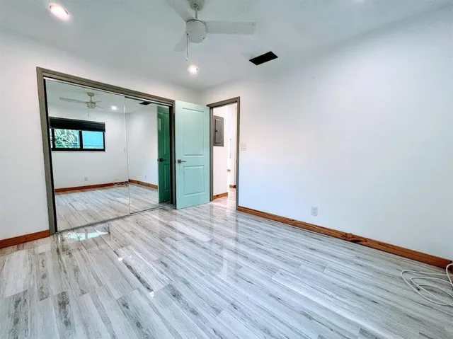 a view of an empty room with wooden floor and a ceiling fan