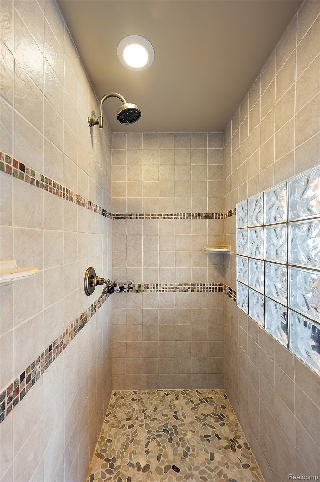 5035 Hidden Ridge Road Metamora, MI 48455 - Photo 33 of 65 Walk-in shower featuring a pebble-tiled floor, light-colored square wall tiles, and decorative mosaic accent bands