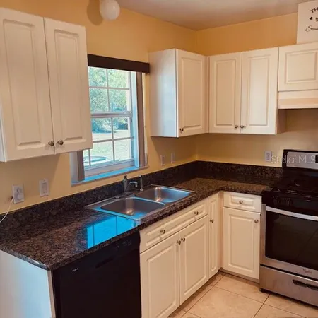 a kitchen with granite countertop a sink dishwasher a stove and white cabinets