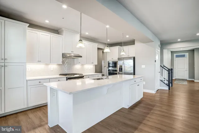 a large kitchen with stainless steel appliances granite countertop a stove a sink a refrigerator and white cabinets with wooden floor