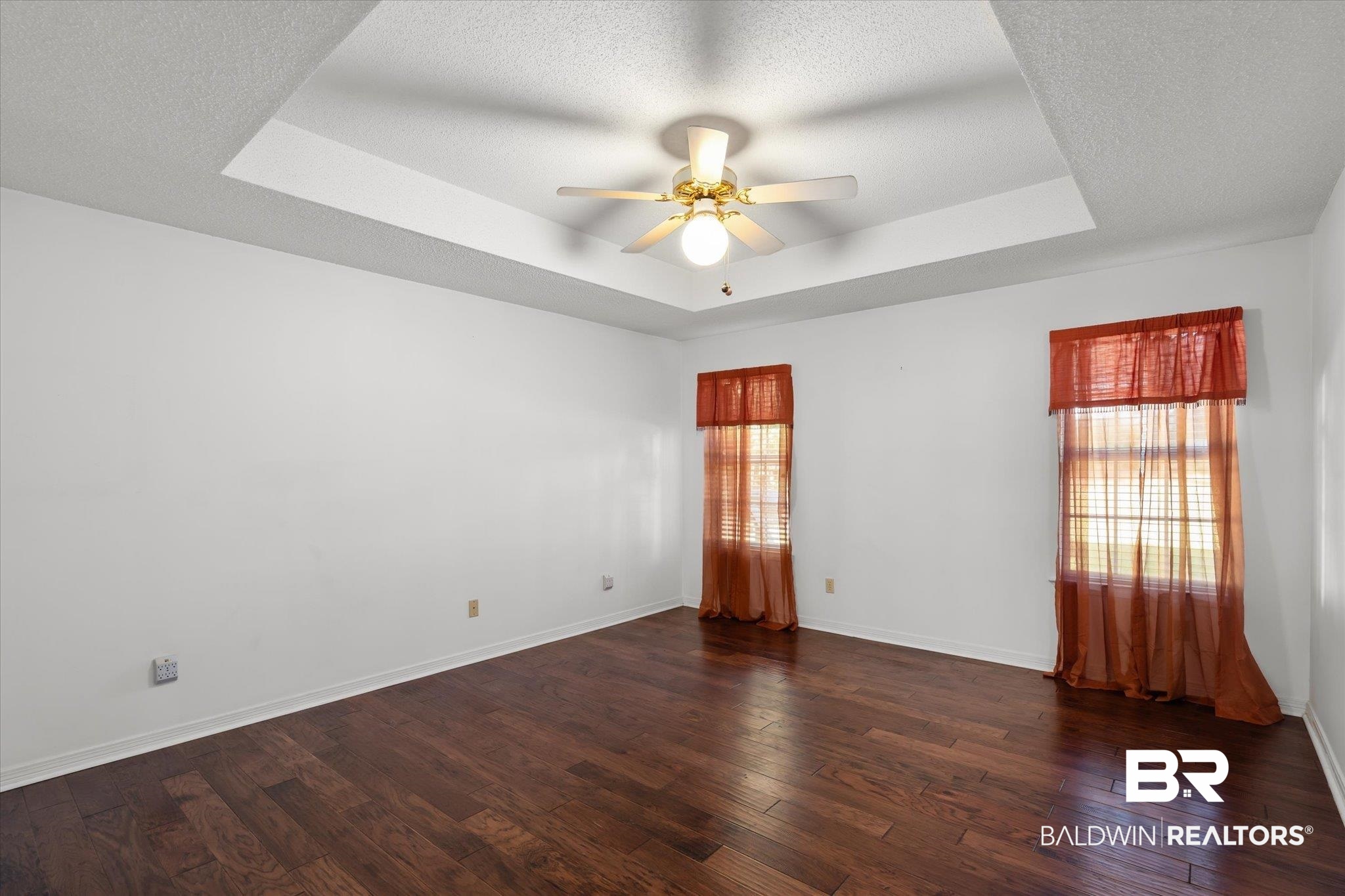7410 East Lakeview Drive Mobile, AL 36695 - Photo 7 of 20 Empty room featuring a raised ceiling, ceiling fan, dark hardwood / wood-style flooring, and a textured ceiling