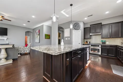 a kitchen with stainless steel appliances granite countertop a sink dishwasher a stove a dining table and chairs with wooden floor