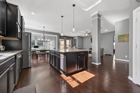 a kitchen with stainless steel appliances kitchen island granite countertop a stove top oven a sink dishwasher a dining table and chairs with wooden floor