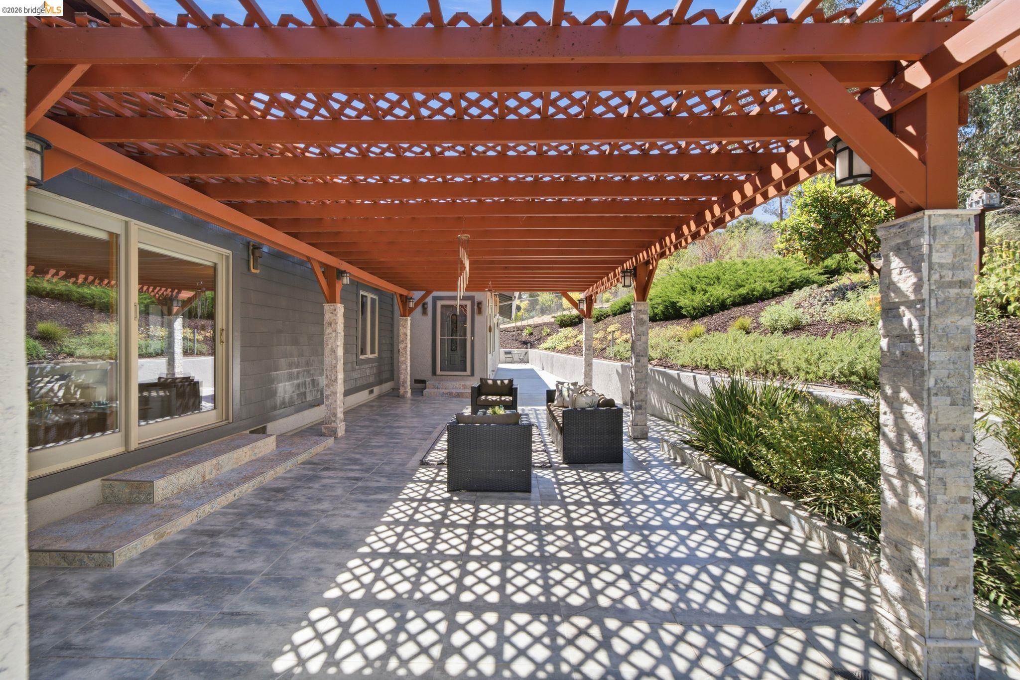 11133 Golf Links Road Oakland, CA 94605 - Photo 46 of 57 Expansive outdoor patio featuring a wooden pergola, patterned tile flooring, sliding glass doors, stone-clad support columns, and built-in exterior lighting